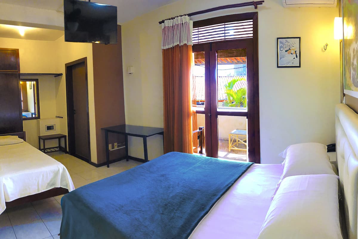 A hotel room with two single beds, a small table, a TV, and a window with curtains.