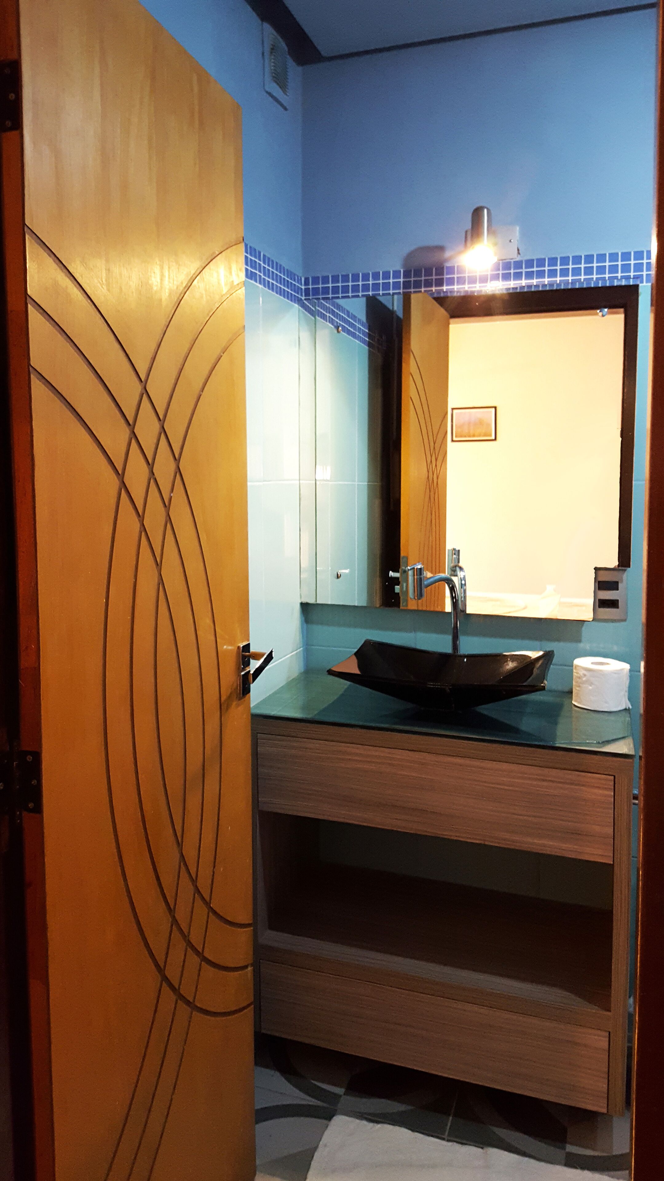 Een badkamer met een houten wastafelmeubel, een zwarte wastafel en een spiegel erboven.