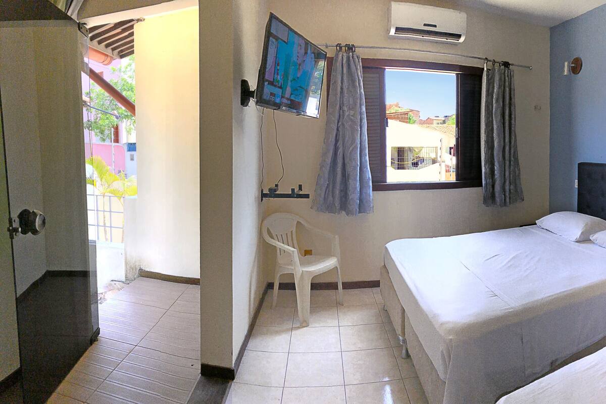 A bedroom with two beds, a TV, a window with curtains, and a chair.