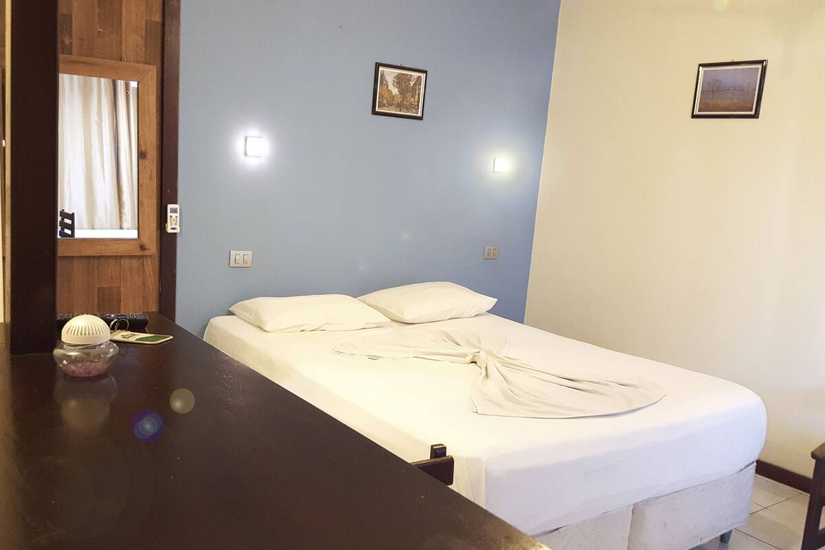 A bedroom with a bed, a wooden table, and two framed pictures on the wall.