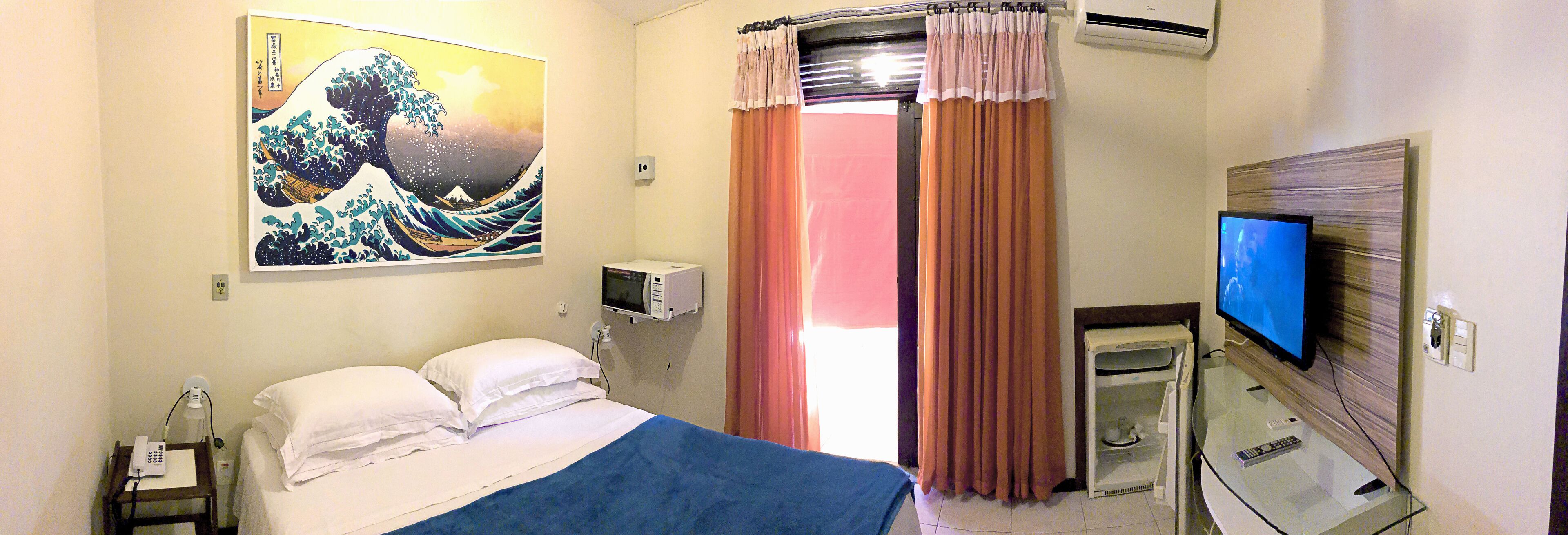 Habitación de hotel con cama, televisor, microondas y un cuadro en la pared.
