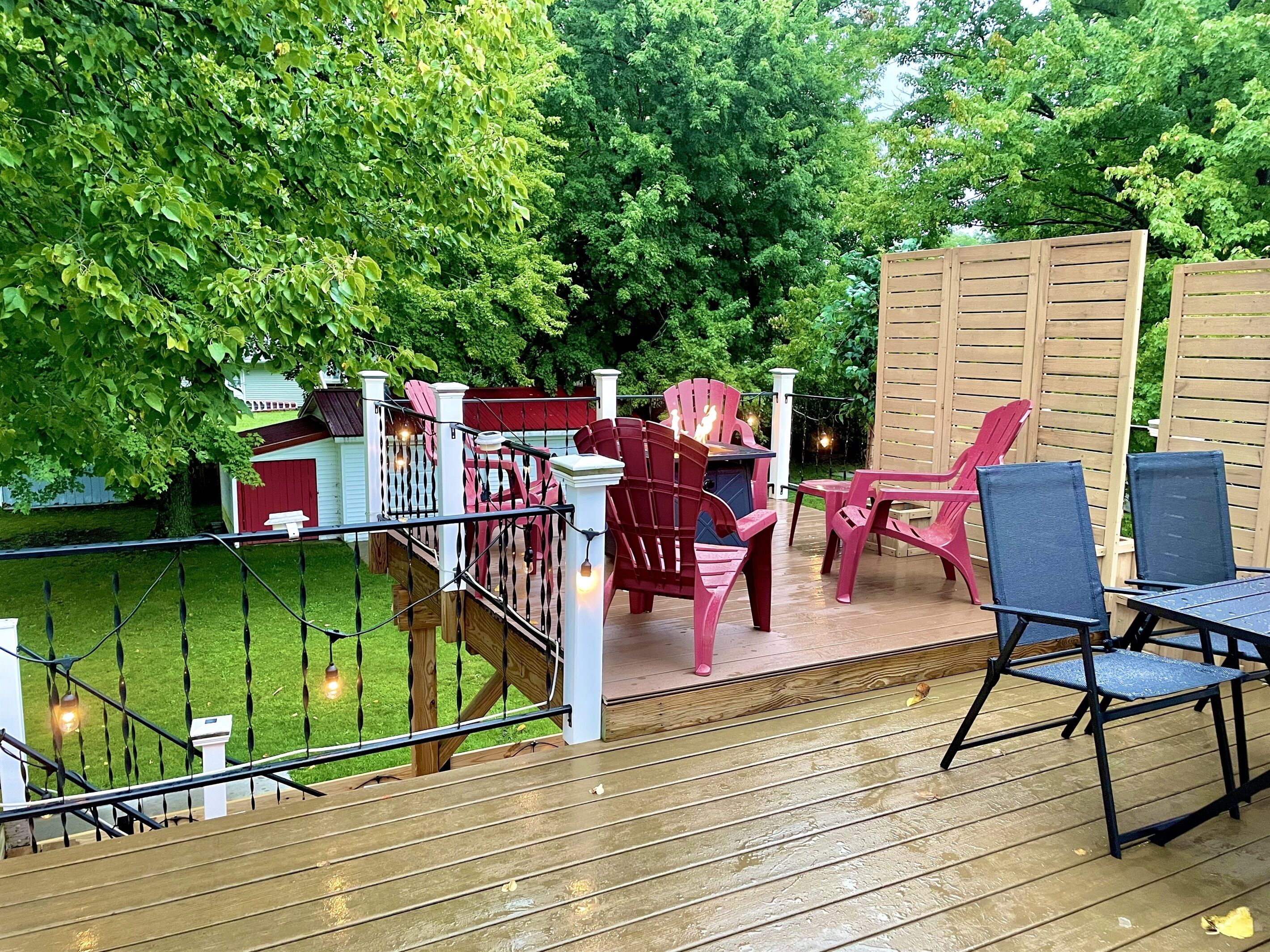A deck with outdoor furniture, including chairs and a table, surrounded by lush greenery.