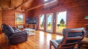 A wooden cabin interior with a sofa, a TV, and a dining area. - SUMMER SPECIALS  Beautiful lake front, beach and pool table (LaPointe)