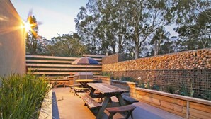 An outdoor patio with picnic tables, a barbecue grill, and a stone wall.