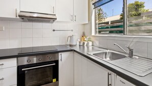 A modern kitchen with white cabinets, a stainless steel range hood, a double sink, and a window providing a view of the outside.