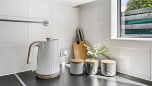 A kitchen counter with a white kettle, wooden cutting board, and three patterned containers.