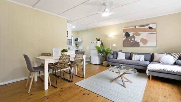 Un salon moderne comprenant un coin repas, un canapé gris, une table basse blanche et un ventilateur de plafond.