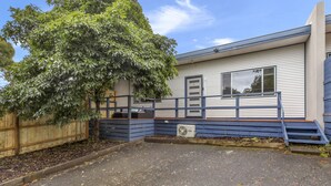 Une maison mobile de plain-pied, avec une façade bleue, une terrasse en bois et un grand arbre devant.