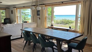 Een ruime woonkamer met een grote houten eettafel, meerdere stoelen, een televisie en uitzicht op de oceaan.