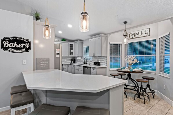 Una cocina moderna con una isla central, taburetes de bar, iluminación colgante y un letrero que dice 'Familia'.