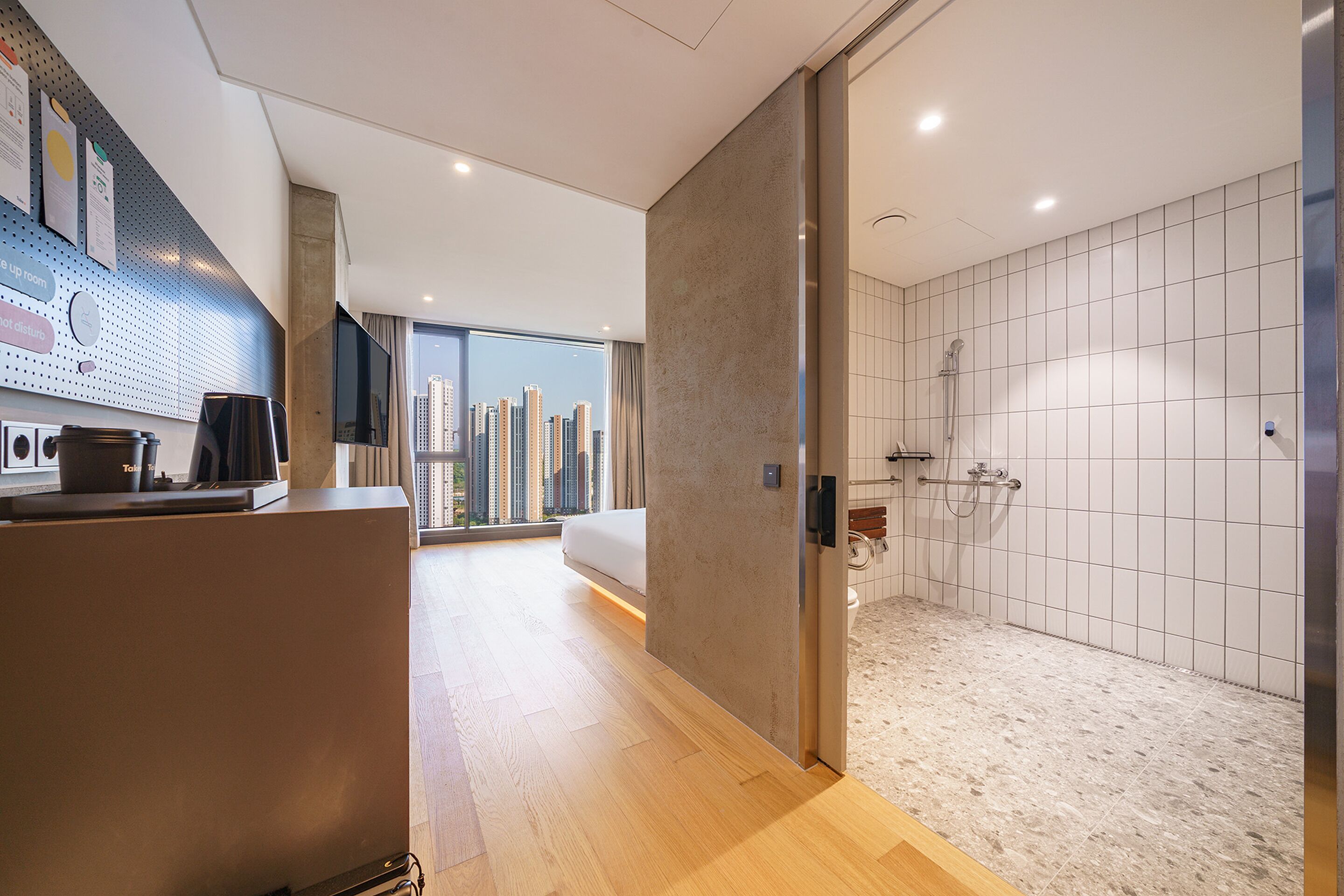 A modern hotel room with a city view, a shower, and a kitchenette.
