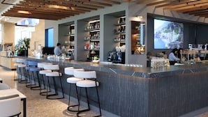 Un área de bar moderna con una barra larga, taburetes y estantes llenos de botellas.