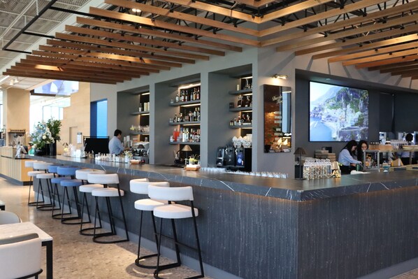 Un área de bar moderna con una barra larga, taburetes y estantes llenos de botellas.