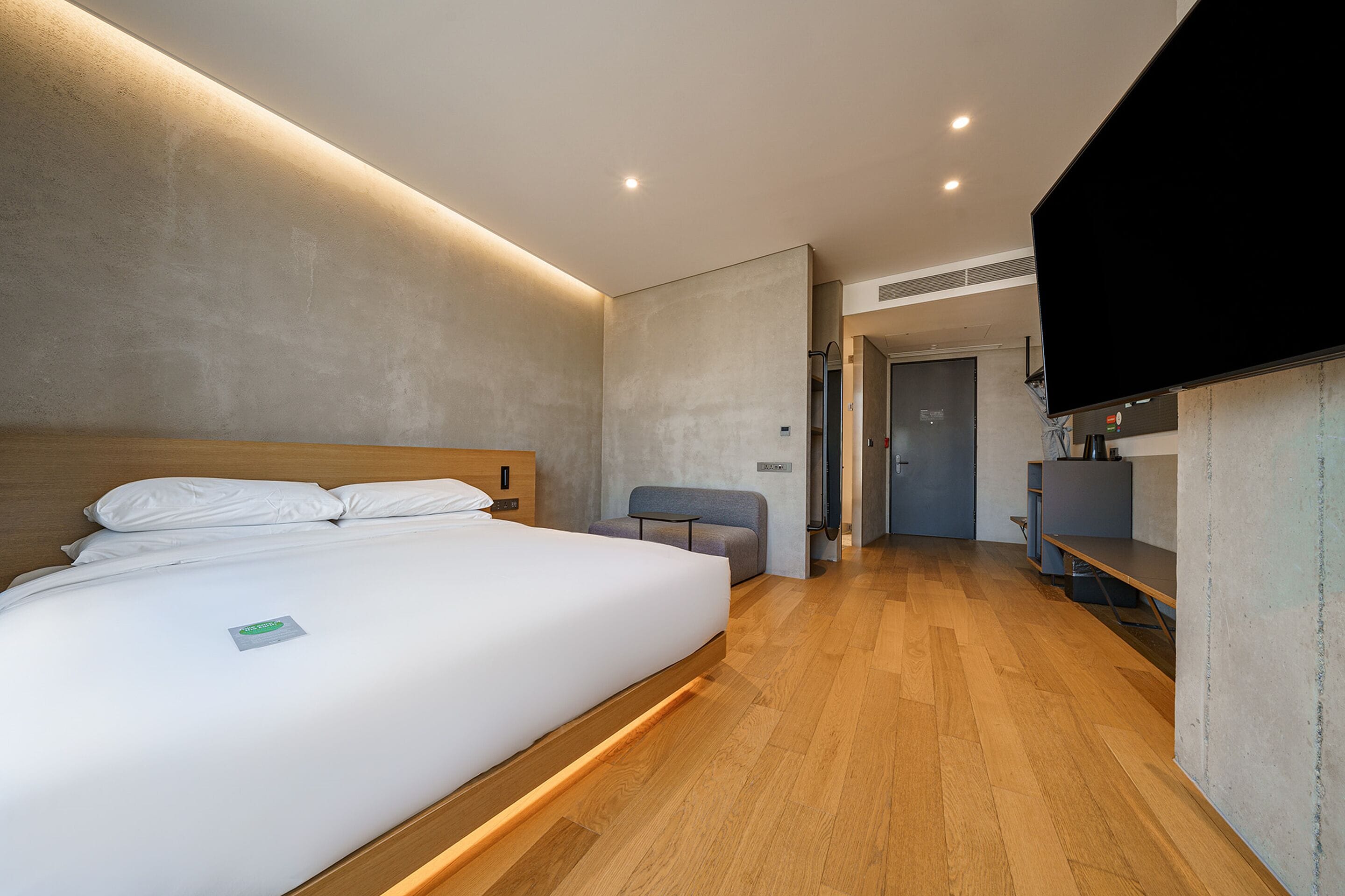 A modern hotel room with a large bed, a seating area, and a flat-screen TV.