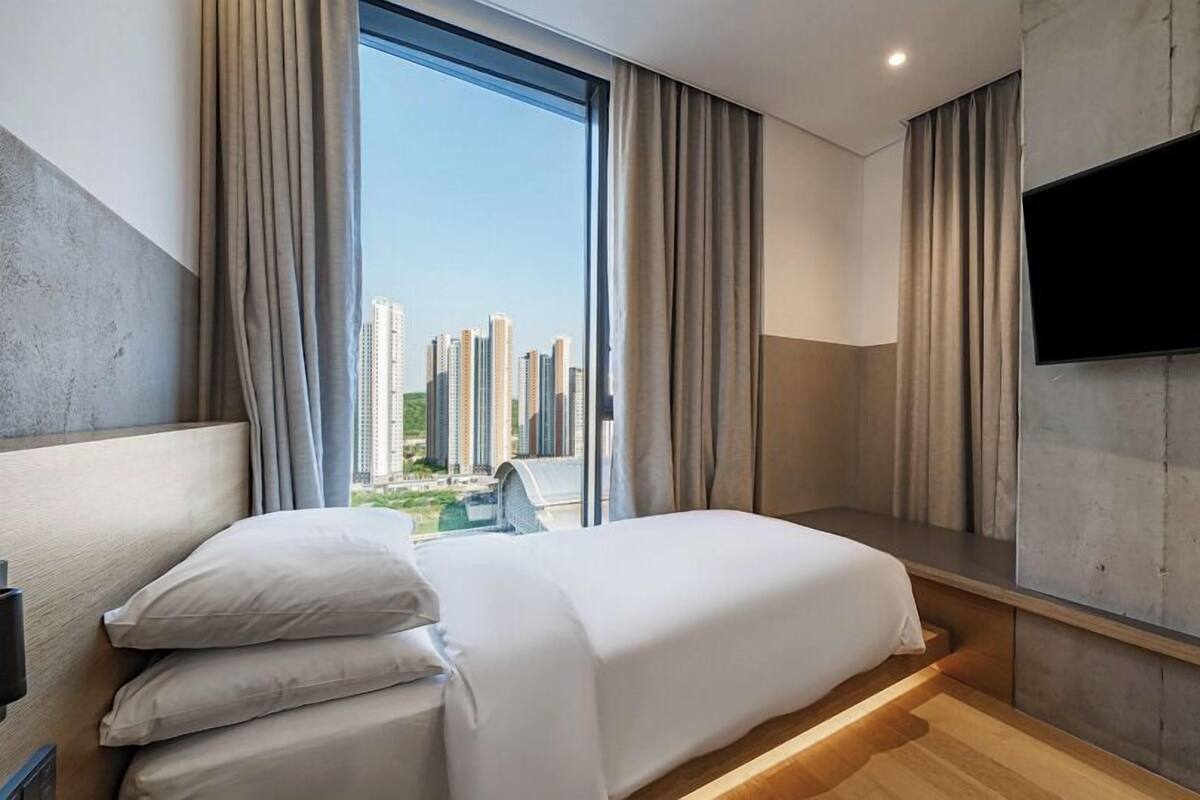 A modern hotel room with a large bed, a flat-screen TV, and a view of high-rise buildings.