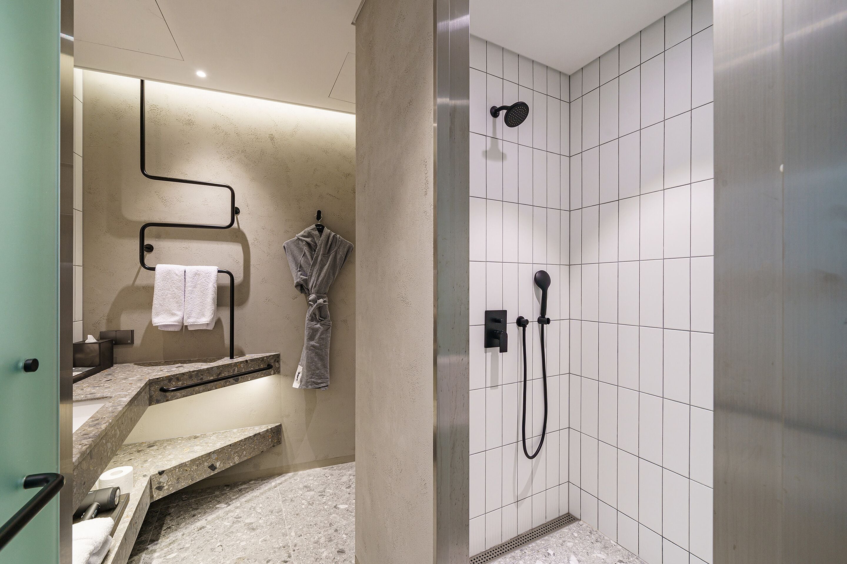 Une salle de bain moderne avec une douche, un meuble-lavabo doté d’un porte-serviettes et un plan de travail en marbre.