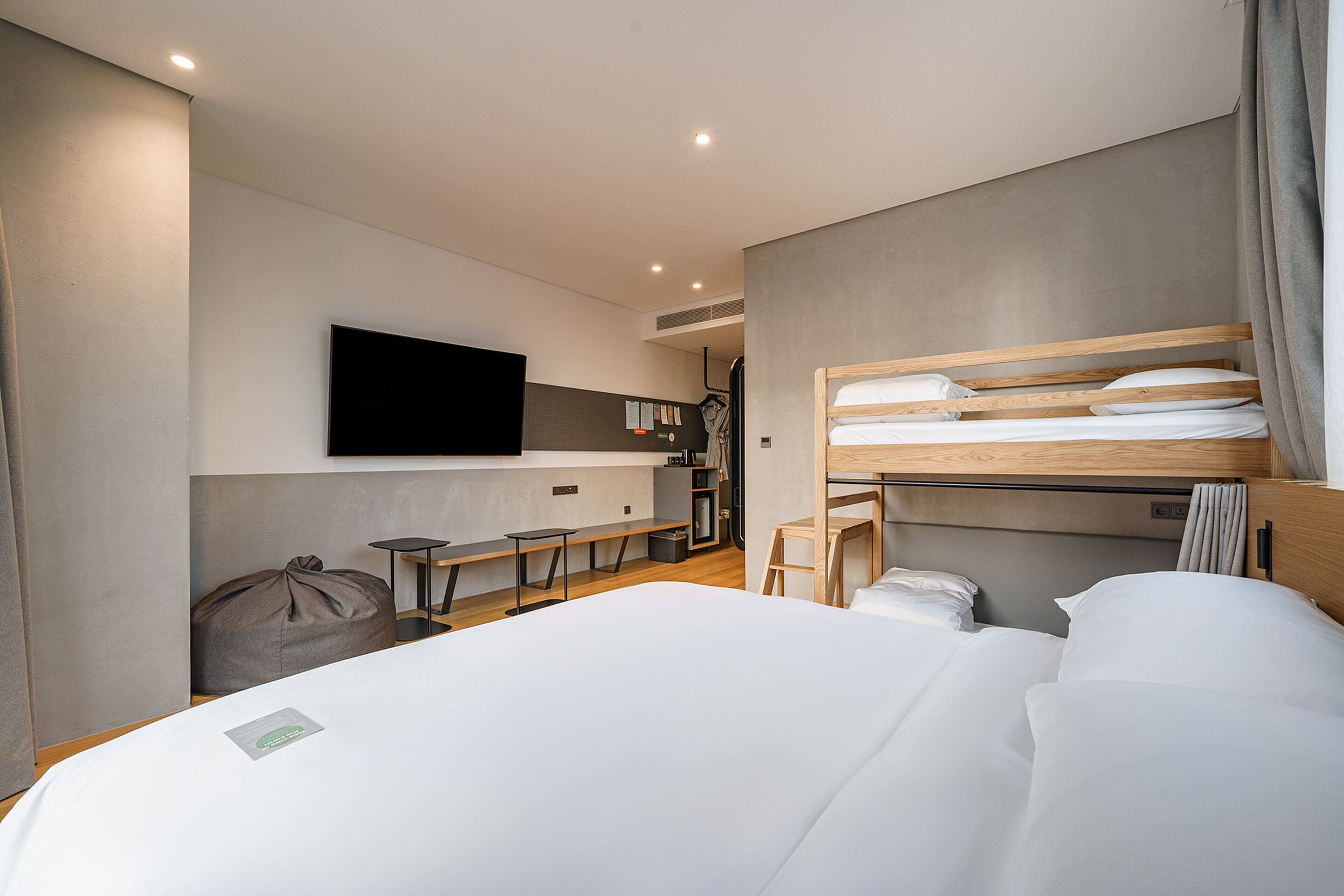 Una habitación de hotel moderna con una cama grande, un televisor de pantalla plana en la pared, un escritorio pequeño y una zona de estar con un sillón de saco y sillas.