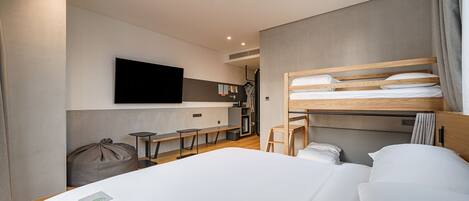 Una habitación de hotel moderna con una cama grande, un televisor de pantalla plana en la pared, un escritorio pequeño y una zona de estar con un sillón de saco y sillas.