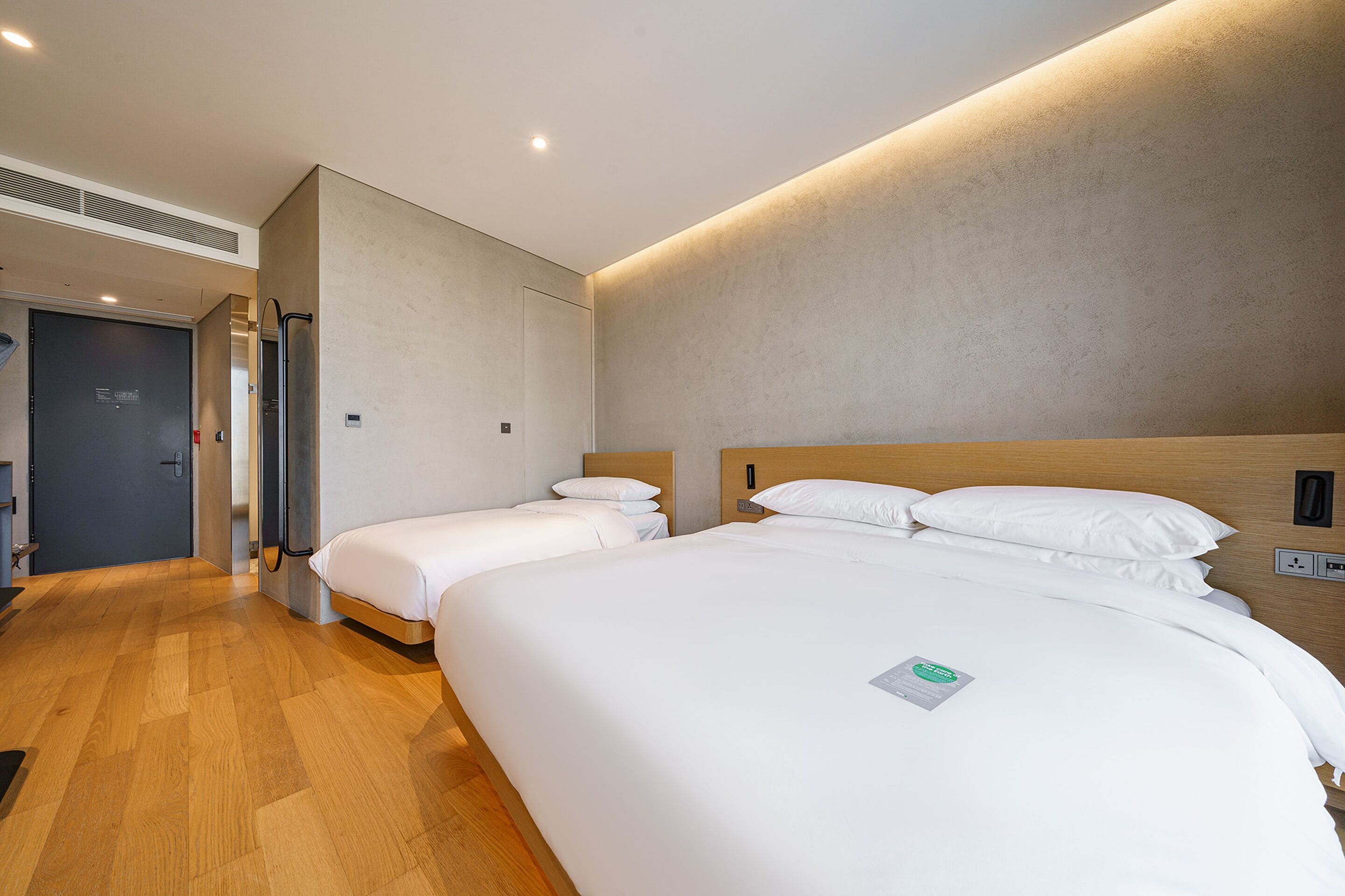 A hotel room with two single beds, a wooden floor, and a modern design.