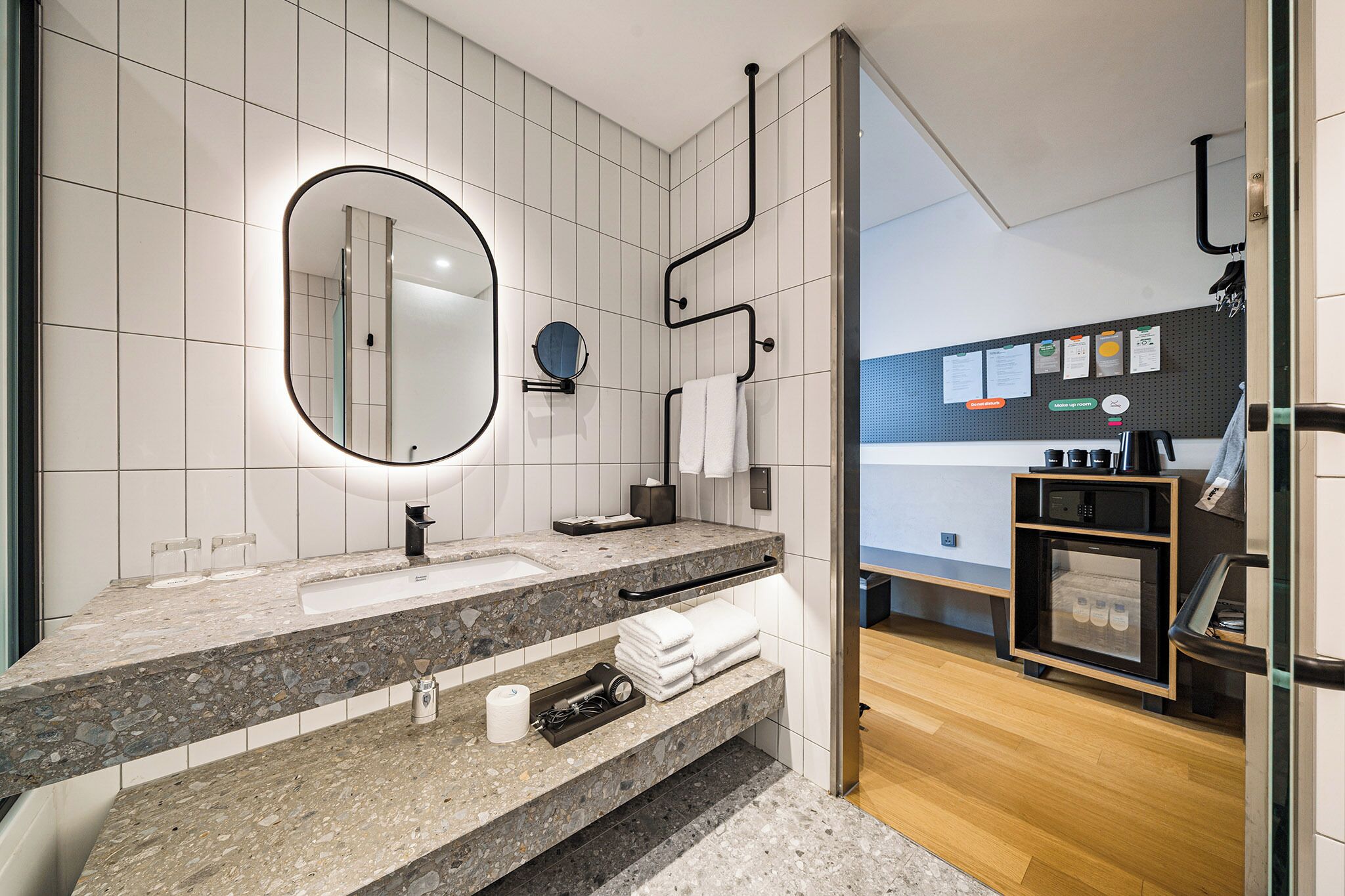Une salle de bain moderne avec un comptoir en granit, un grand miroir, un porte-serviettes et un petit réfrigérateur.