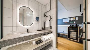 Une salle de bain moderne avec un comptoir en granit, un grand miroir, un porte-serviettes et un petit réfrigérateur.