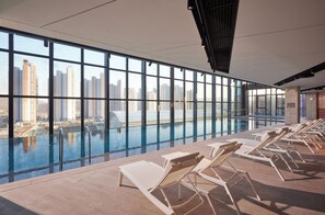Piscina infinita en la azotea con sillones de descanso, ventanas amplias y vistas a rascacielos.