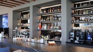 Zona de bar con estantes llenos de botellas de licores, una máquina de café y una pantalla de televisión.