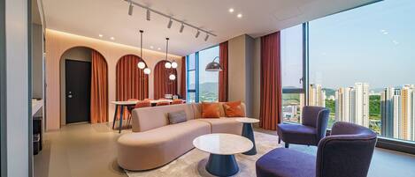 A modern living room with a sofa, two armchairs, a coffee table, and a dining area with a table and chairs. Large windows offer a city view.