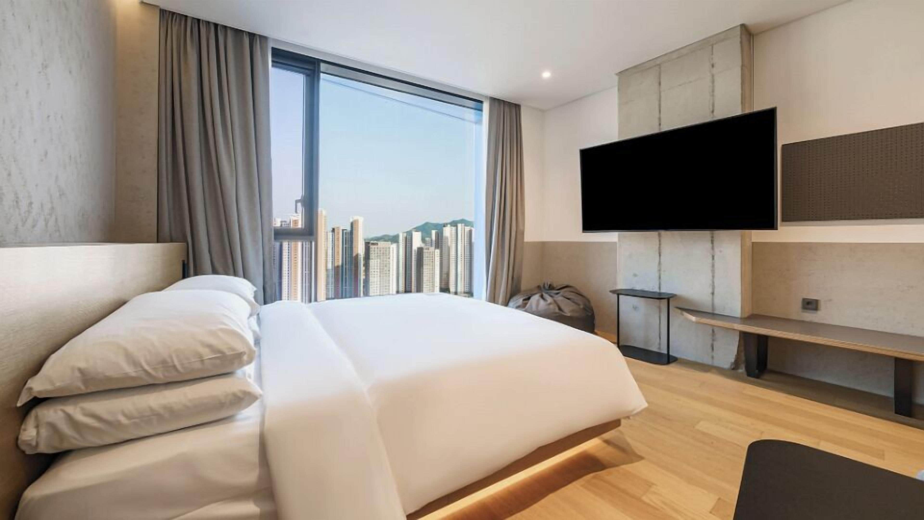 A modern hotel room with a large bed, a TV mounted on the wall, and a city view.