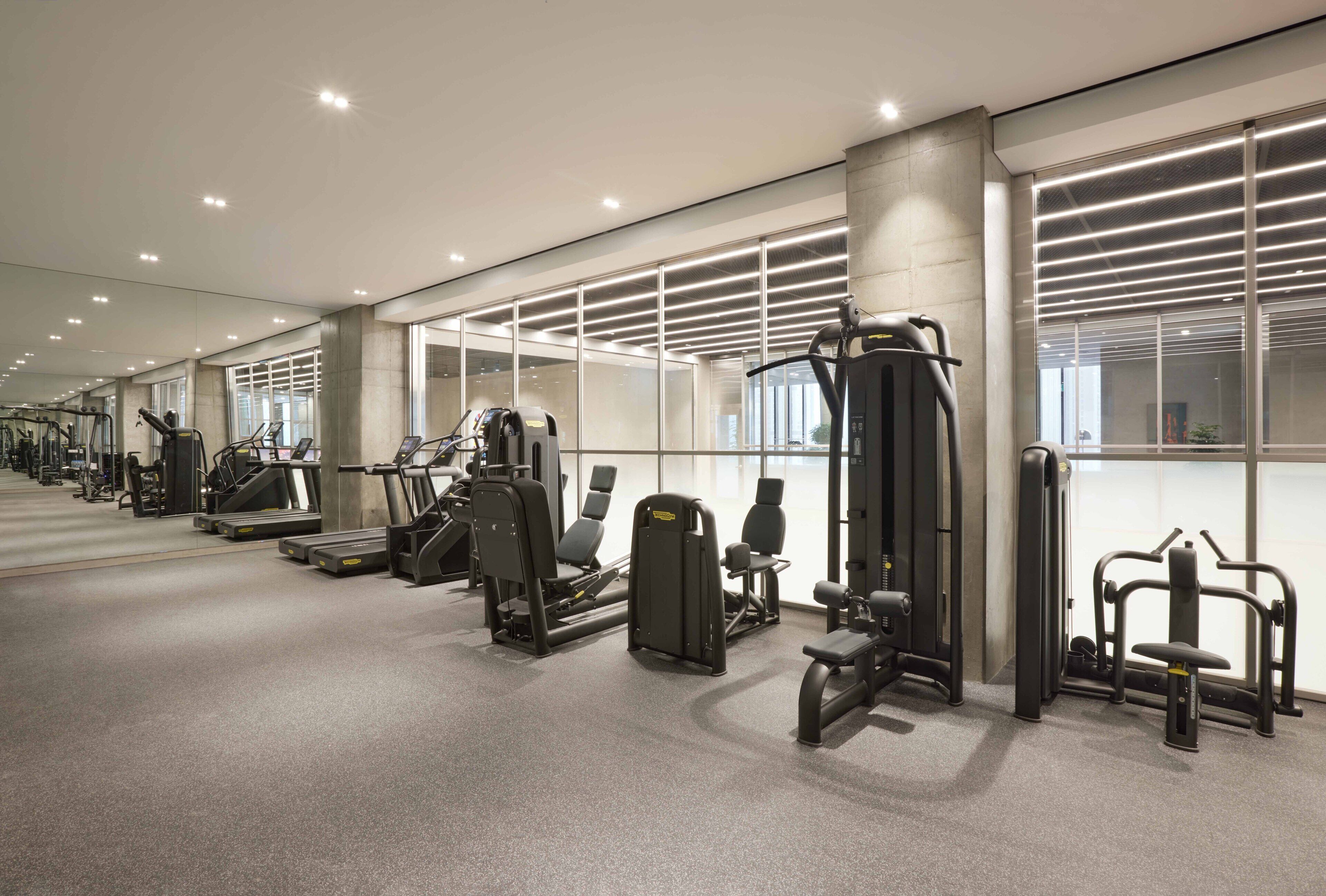 A modern gym with various exercise machines, large windows, and a clean, well-lit interior.