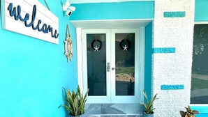 A turquoise exterior with a 'Welcome' sign, two potted plants, and a door with starfish decorations. - LILY'S BEACH HOUSE - POOL HOUSE WITH DIRECT RIVER ACCESS (Cape Coral)