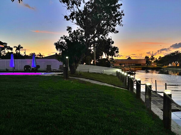 A grassy area with a pool, umbrellas, and a fence. - LILY'S BEACH HOUSE - POOL HOUSE WITH DIRECT RIVER ACCESS (Cape Coral)