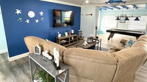 A living room with a blue accent wall, a large beige sofa, a flat-screen TV, and a ceiling fan. - LILY'S BEACH HOUSE - POOL HOUSE WITH DIRECT RIVER ACCESS (Cape Coral)