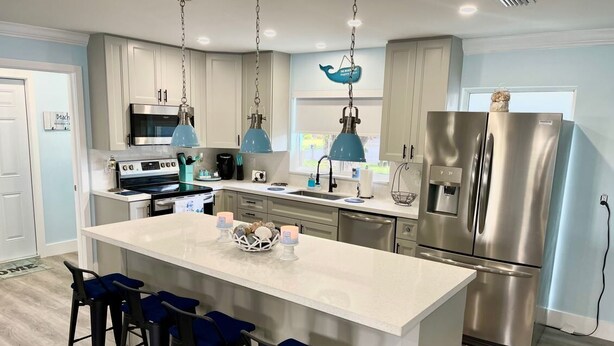 A modern kitchen with a central island, stainless steel appliances, and blue pendant lights. - LILY'S BEACH HOUSE - POOL HOUSE WITH DIRECT RIVER ACCESS (Cape Coral)