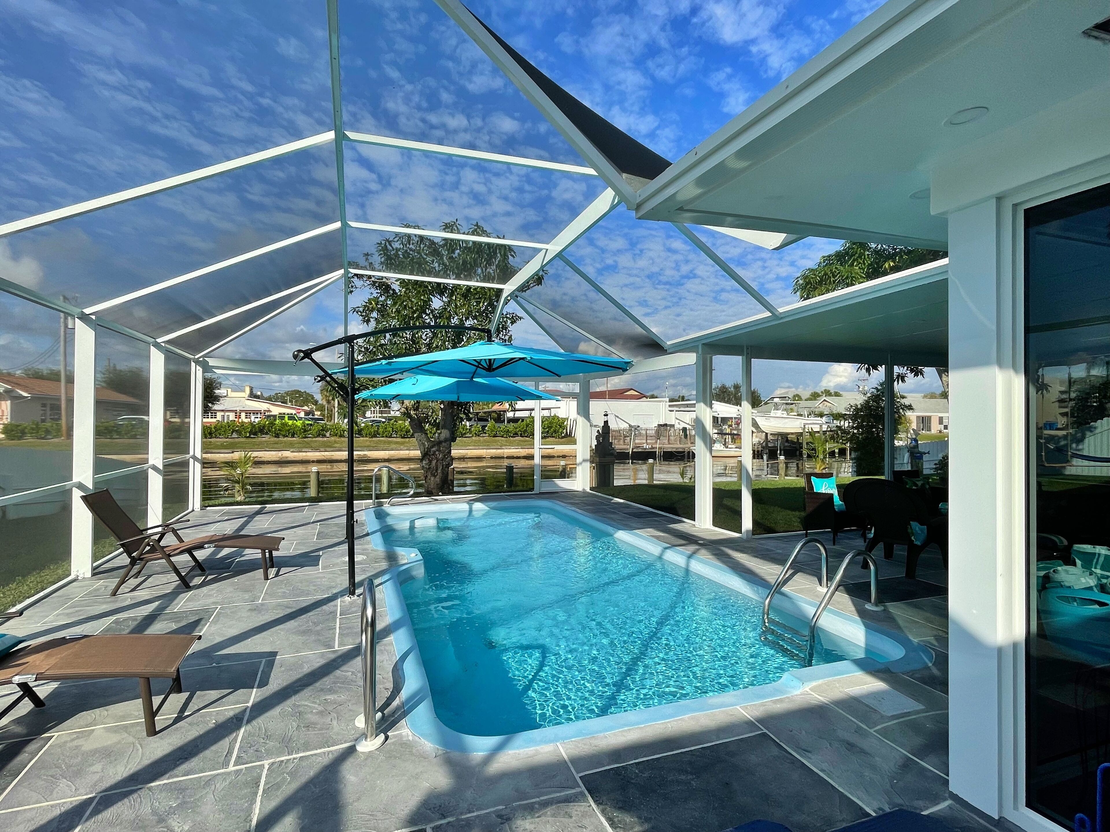 Une piscine extérieure couverte, dotée de chaises longues et d’un parasol bleu.
