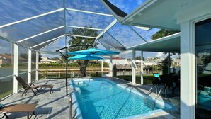 A covered outdoor swimming pool with lounge chairs and a blue umbrella. - LILY'S BEACH HOUSE - POOL HOUSE WITH DIRECT RIVER ACCESS (Cape Coral)