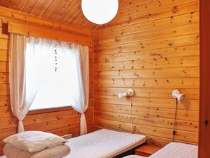 Una camera in una baita di legno con due letti, una finestra con tende e un lampadario a parete.