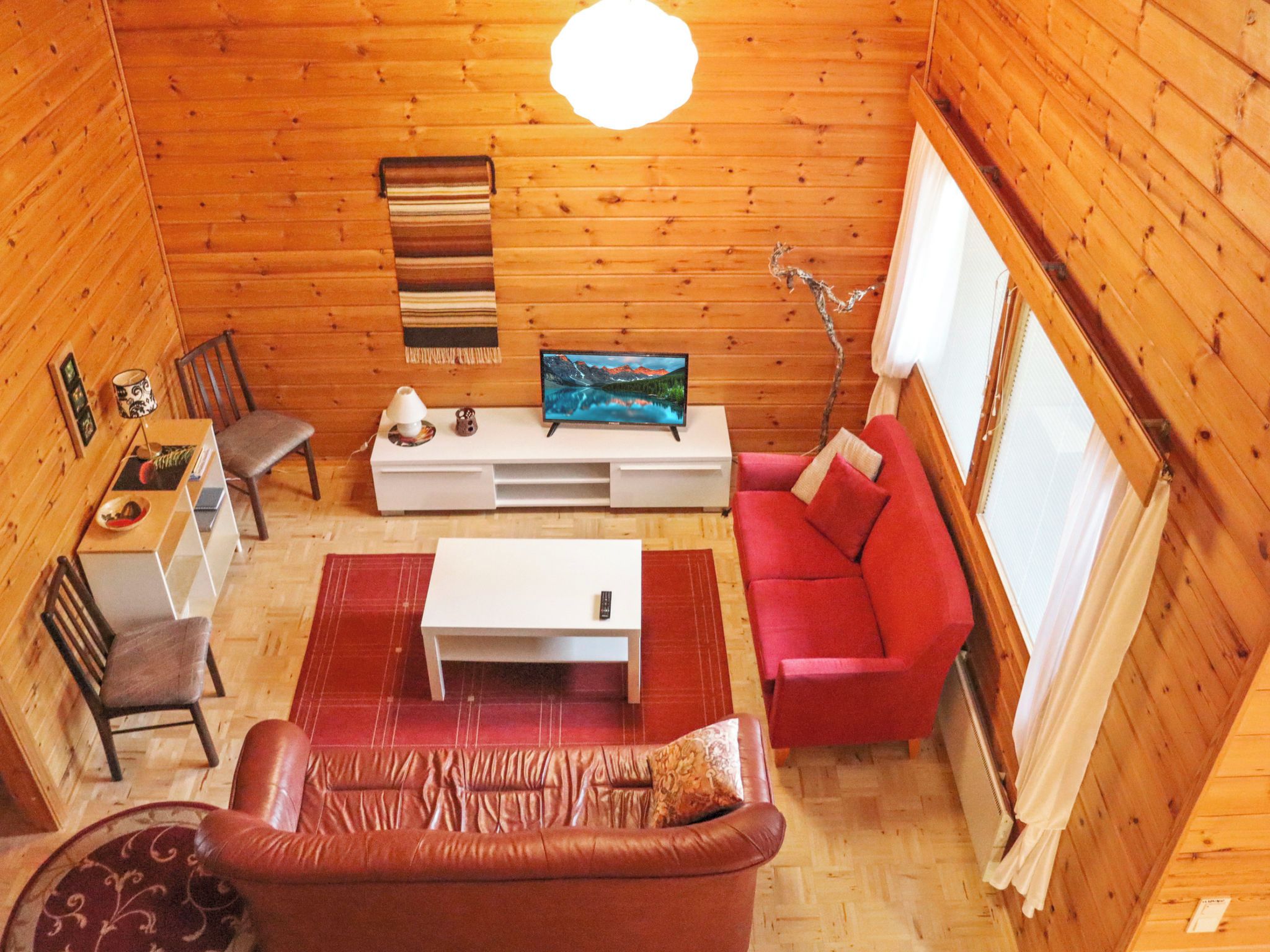 Une pièce chaleureuse avec un canapé en cuir, un divan rouge, un meuble TV blanc et un plafond en bois.