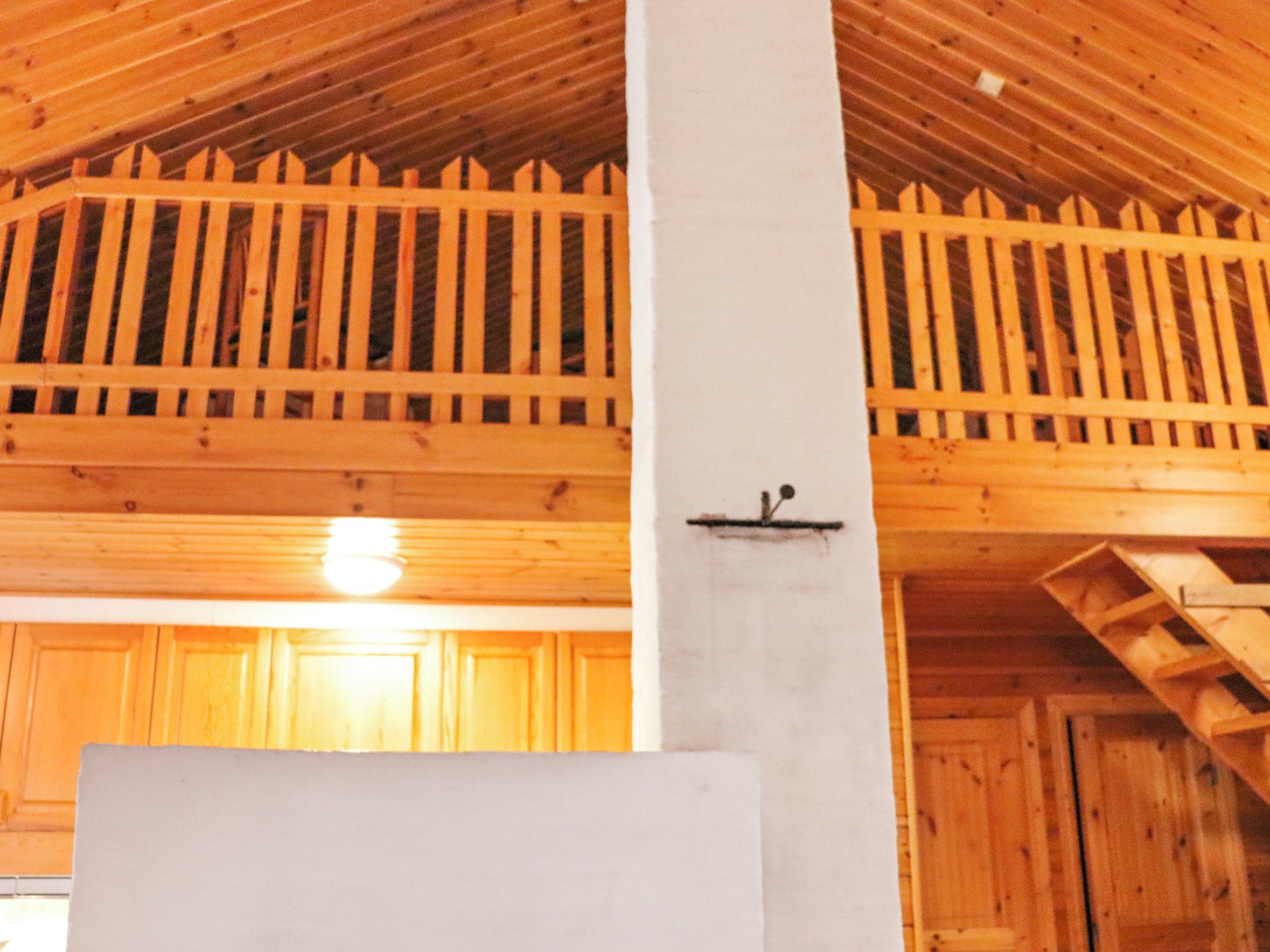 Un intérieur en bois avec un plafond haut, un pilier blanc et un escalier en bois.