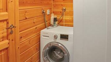 A compact, white washing machine in a wooden-paneled room with a door.