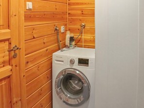 A compact, white washing machine in a wooden-paneled room with a door.