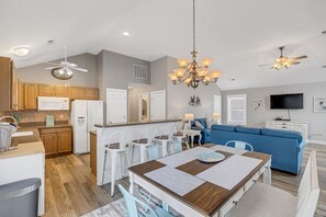 Cozinha moderna com eletrodomésticos brancos, sala de jantar com mesa de madeira e sofá azul na sala de estar.