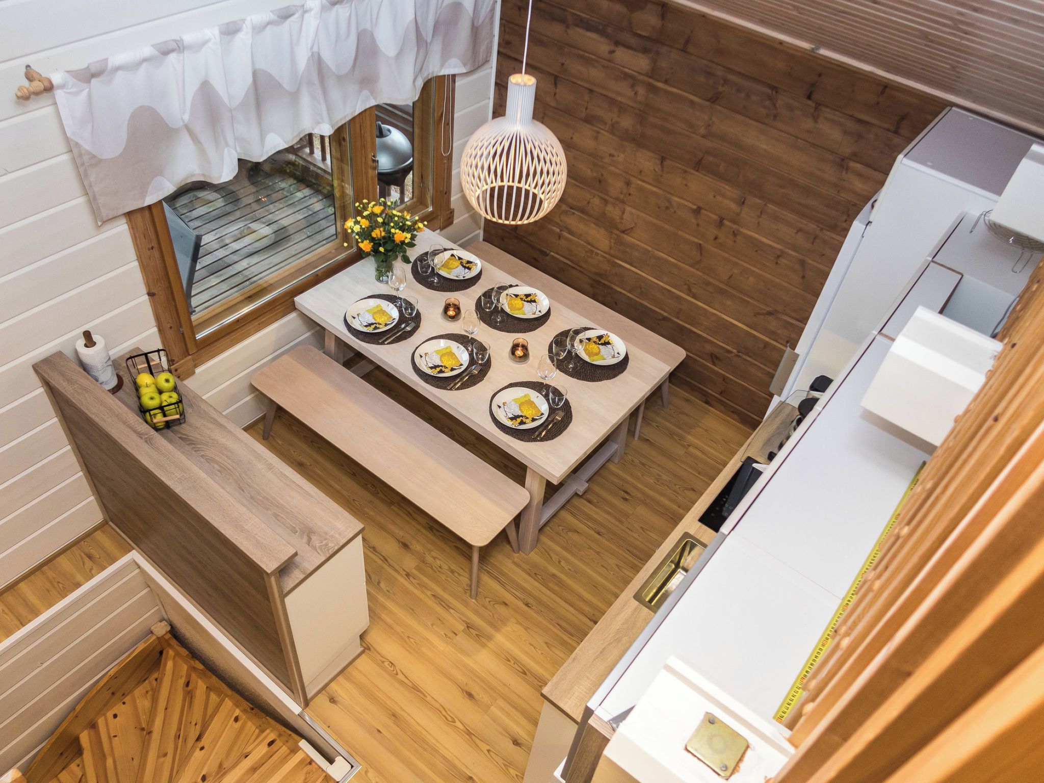 A compact kitchen with a dining area, wooden flooring, and a hanging light fixture.