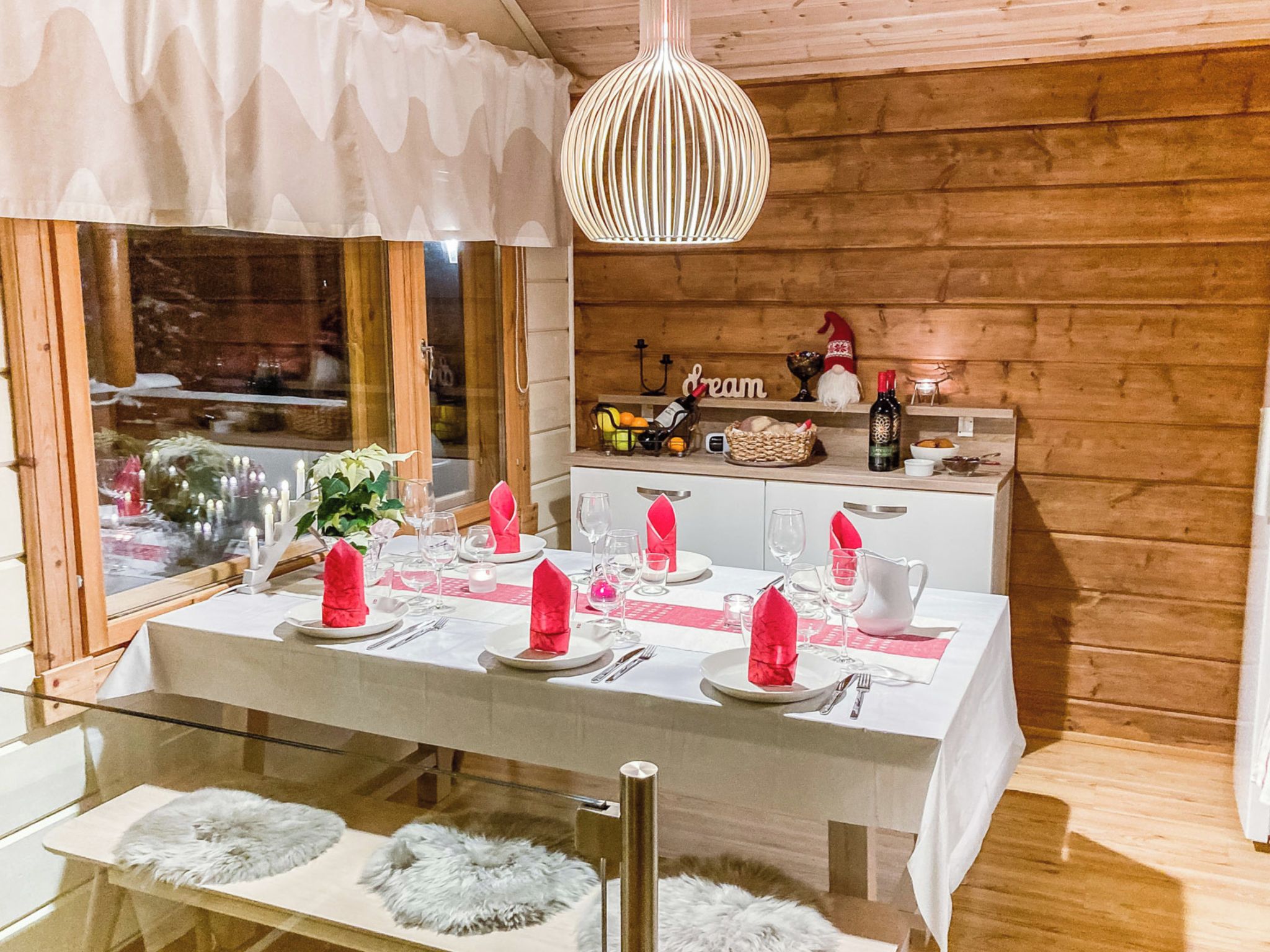 A dining area with a wooden interior, a table set for four with pink napkins, and a hanging light fixture above.