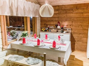 Un comedor con interior de madera, una mesa dispuesta para cuatro personas con servilletas rosas, y una lámpara colgante encima.