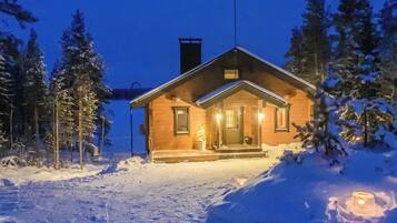 A wooden cabin with a porch, surrounded by snow-covered trees.