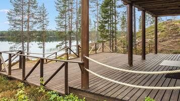 Une terrasse en bois, délimitée par une barrière en corde, qui offre une vue sur un lac paisible et est entourée d’arbres.
