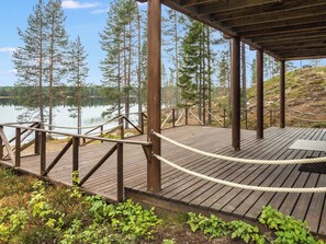 A wooden deck with a rope barrier, overlooking a calm lake and surrounded by trees. - Pähkinä by Interhome (Kuusamo)
