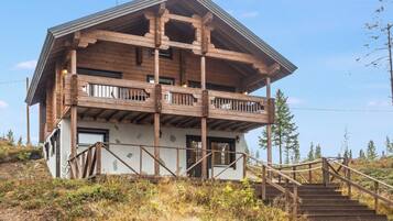A two-story wooden cabin with a balcony, surrounded by natural vegetation.