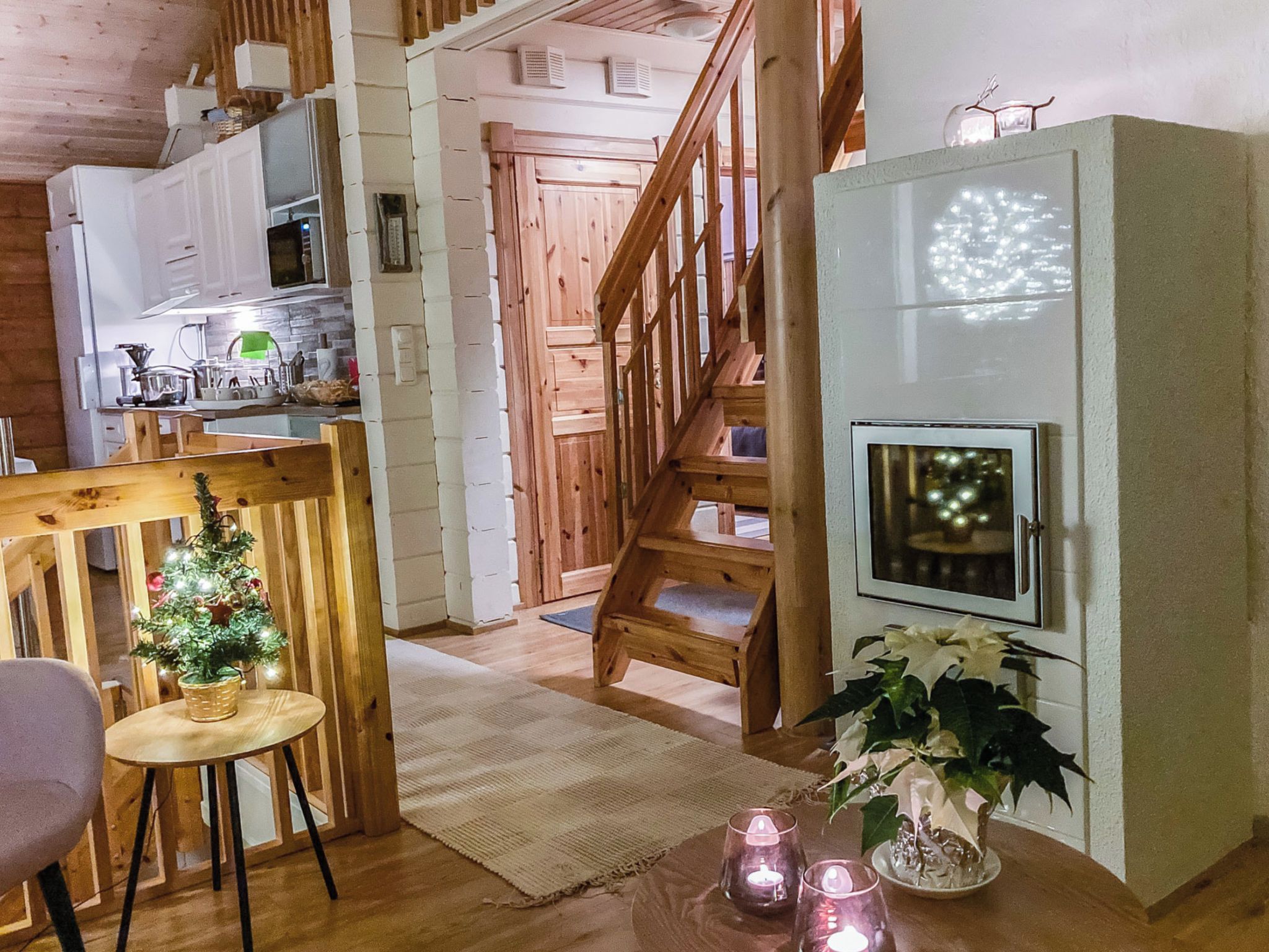Un intérieur chaleureux avec un escalier en bois, un coin repas agrémenté d’un petit sapin de Noël et une cuisine équipée d’appareils modernes.